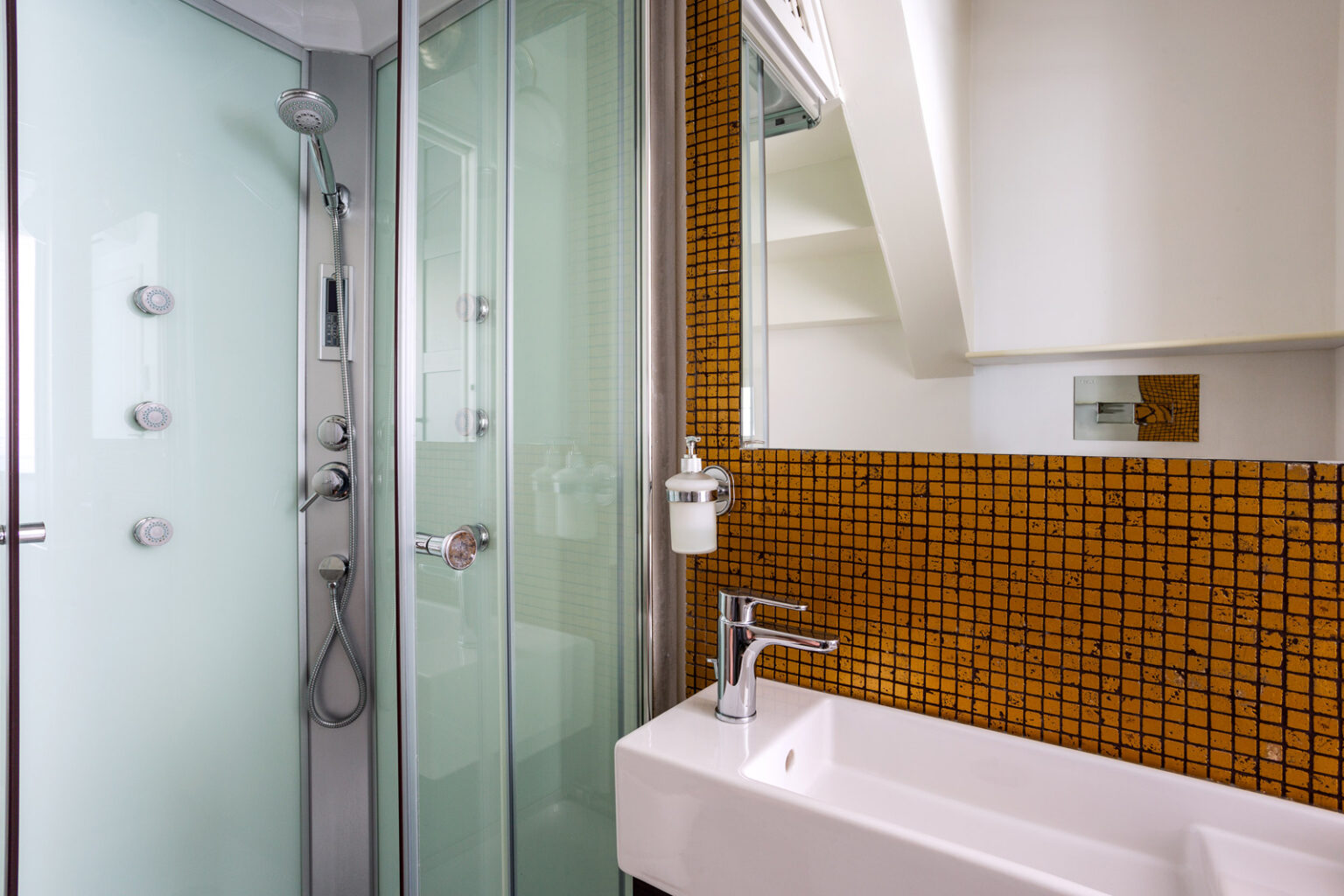 Modern bathroom featuring a glass shower enclosure, sleek white bathtub, and vibrant orange mosaic tile wall. The space is well-lit with a minimalist design and contemporary fixtures. | Only on SopranoVillas