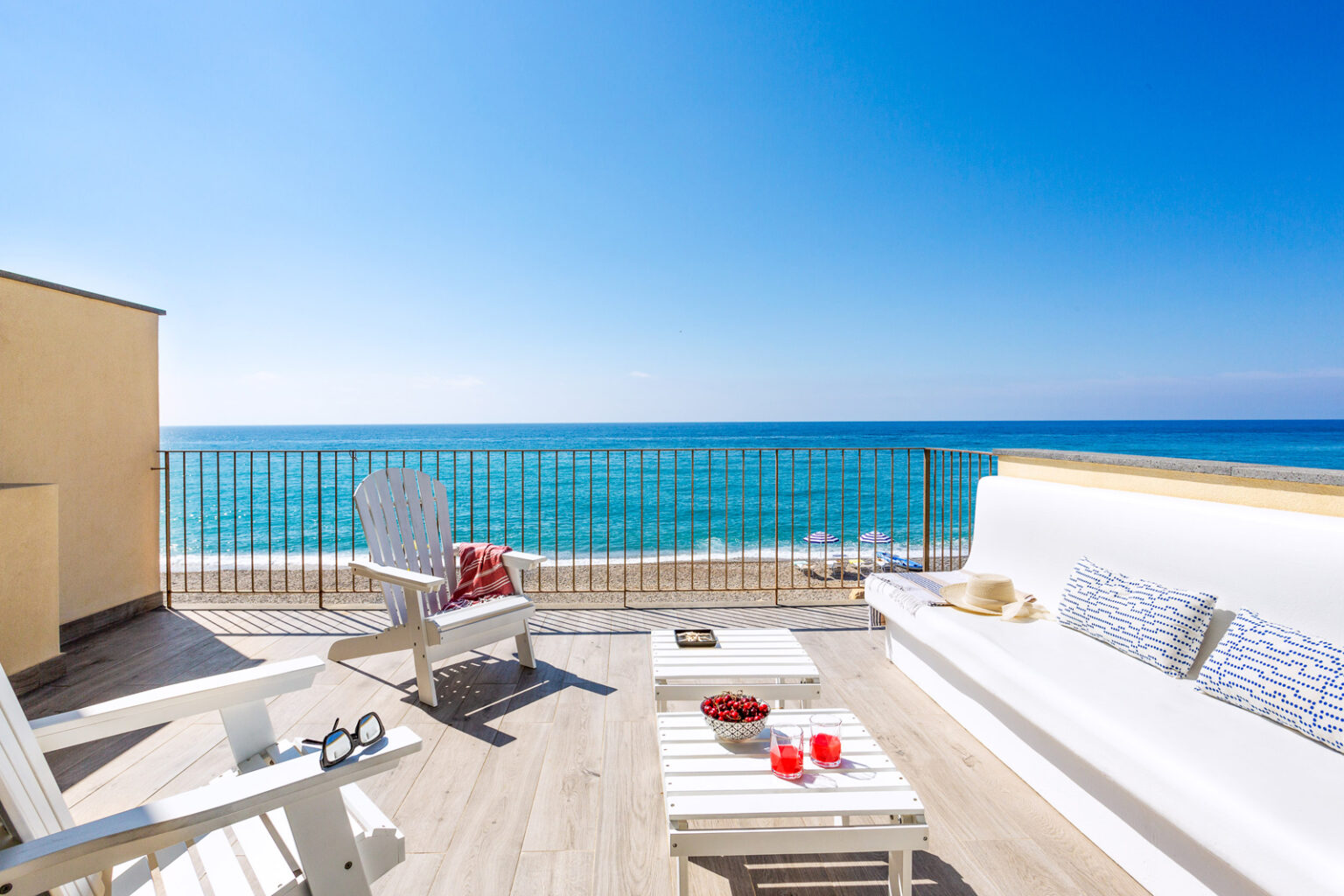 Cozy seaside balcony featuring white outdoor furniture, a stunning ocean view, and refreshing drinks, perfect for relaxation and enjoying the beach atmosphere. | Only on SopranoVillas