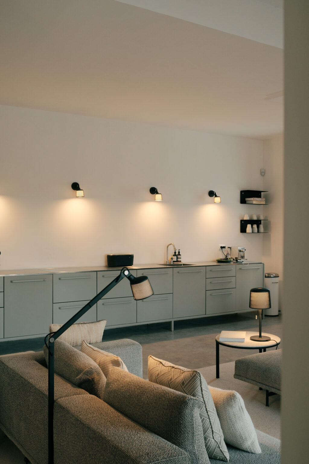 Modern kitchen interior featuring sleek gray cabinetry, minimalist wall-mounted lighting, and stylish shelving with kitchenware. The design emphasizes functionality and contemporary aesthetics. | Only on SopranoVillas