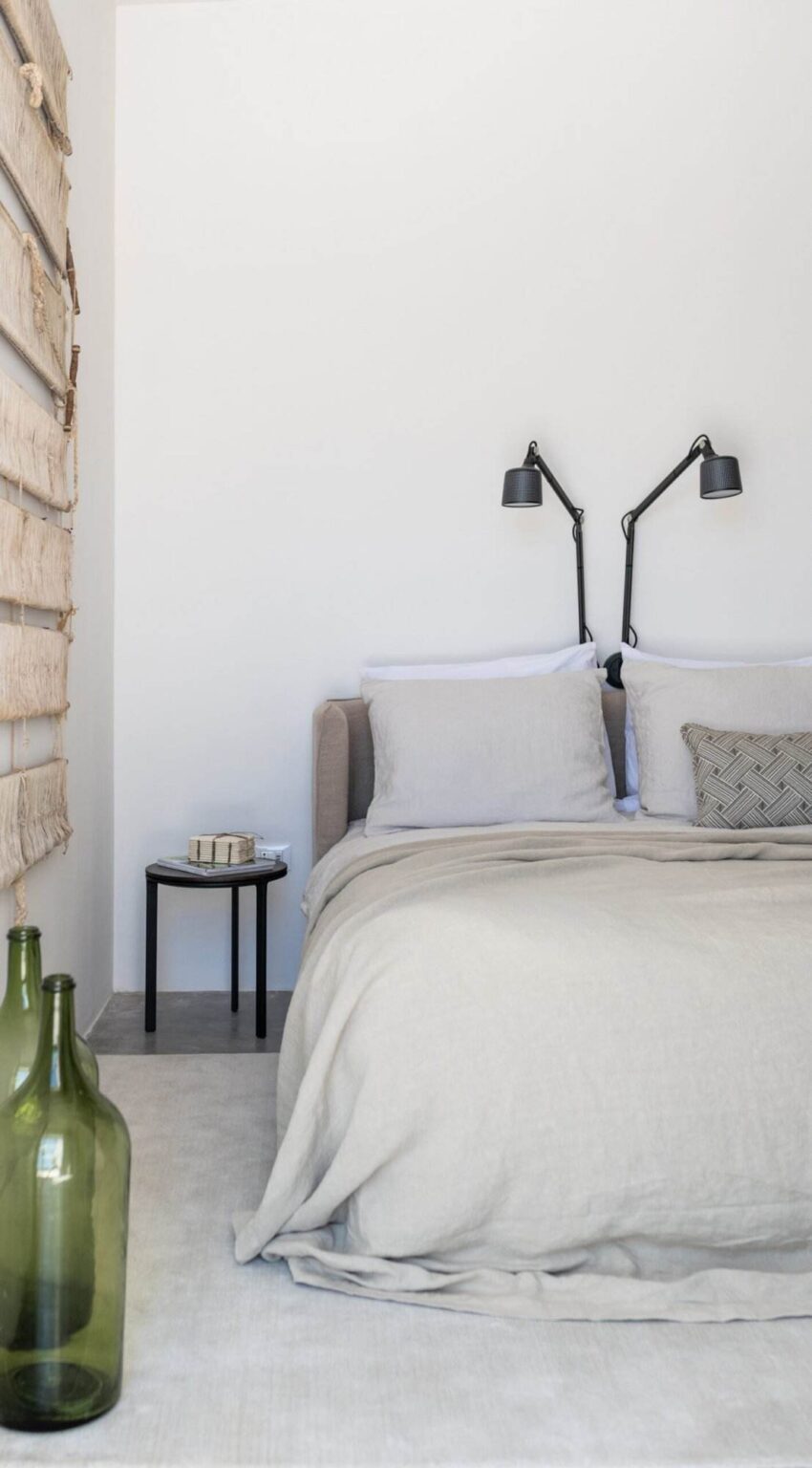 Modern bedroom design featuring a cozy bed with neutral bedding, stylish wall-mounted lamps, and a minimalist bedside table. The decor emphasizes simplicity and elegance, creating a serene atmosphere. | Only on SopranoVillas