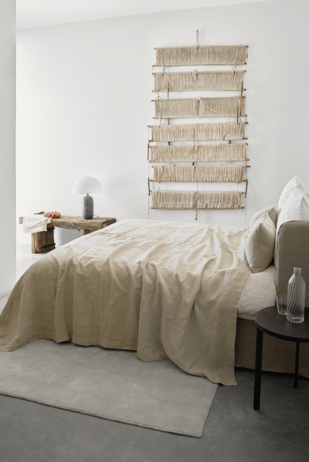 Modern bedroom with a beige linen bedspread, decorative wall hanging, minimalist lamp, and rustic wooden bench, creating a serene and stylish atmosphere. | Only on SopranoVillas