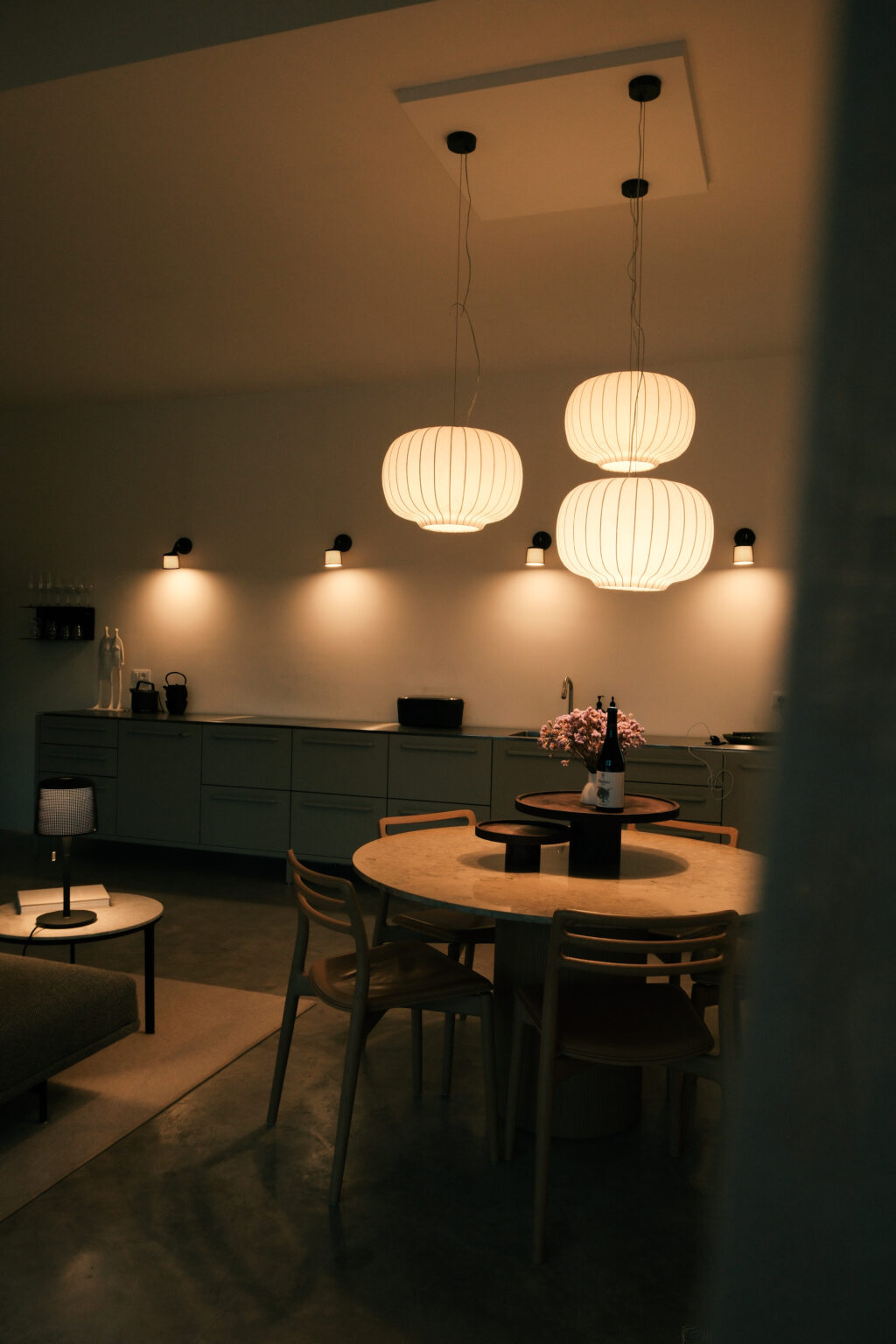 Modern kitchen interior featuring stylish pendant lights, a round dining table with a floral centerpiece, and neutral cabinetry, creating a warm and inviting atmosphere. | Only on SopranoVillas