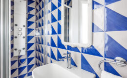 Modern bathroom featuring a stylish shower with a sleek panel and multiple showerhead options, complemented by a vibrant blue and white geometric tile design. A contemporary sink with a chrome faucet and a decorative mirror enhance the space's aesthetic appeal.