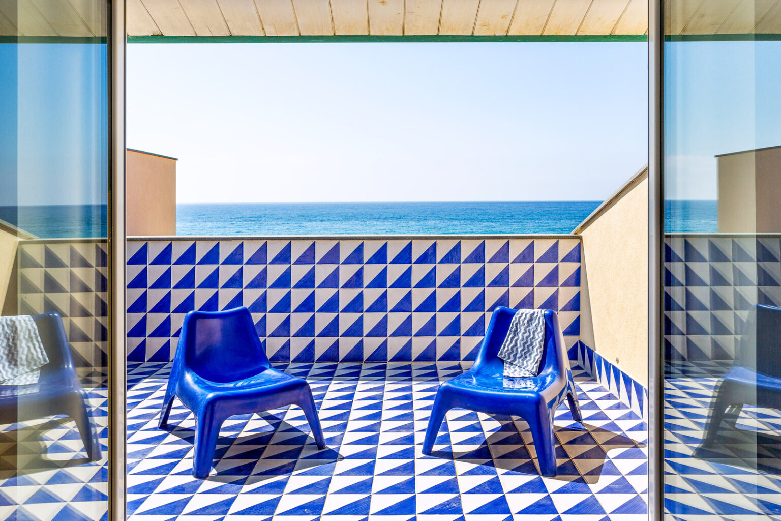Bright coastal balcony with blue chairs and patterned tile flooring overlooking the ocean. Perfect for relaxation and enjoying sea views. | Only on SopranoVillas