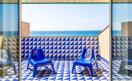 Bright coastal balcony with blue chairs and patterned tile flooring overlooking the ocean. Perfect for relaxation and enjoying sea views.