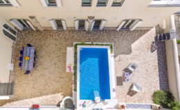 Aerial view of a modern outdoor patio featuring a rectangular swimming pool, surrounded by potted plants and stylish seating. A colorful dining table is set for outdoor meals, highlighting the inviting atmosphere of this luxurious outdoor space.