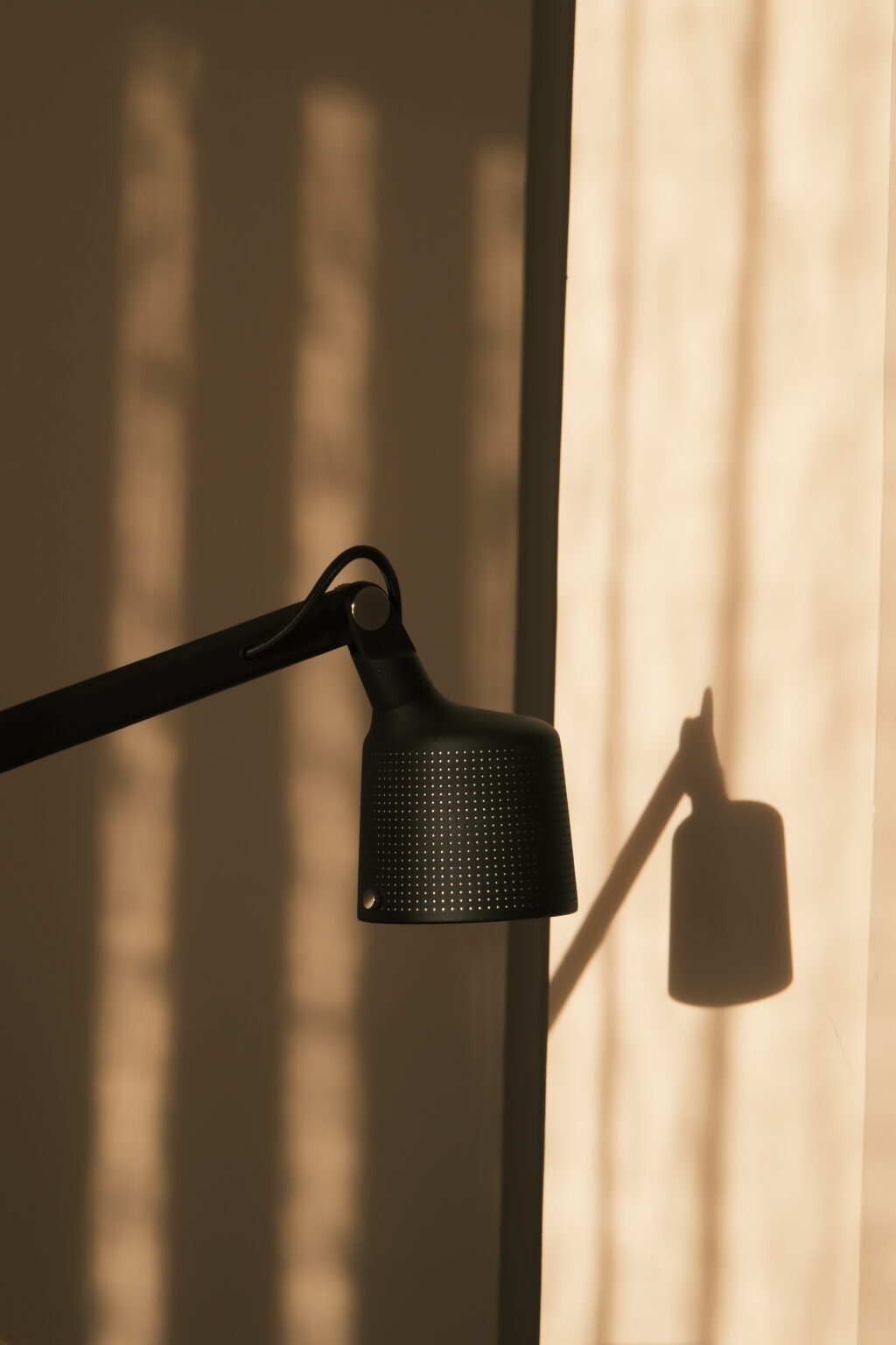 Black desk lamp casting a shadow on a beige wall, showcasing a modern design and warm lighting. | Only on SopranoVillas