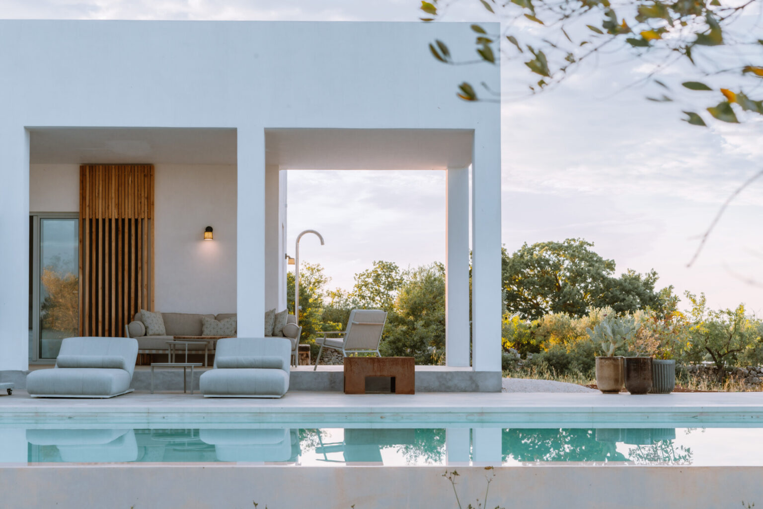 Modern villa exterior with a swimming pool, featuring minimalist design elements, outdoor seating, and lush greenery in the background. Ideal for luxury vacation rentals and contemporary architecture enthusiasts. | Only on SopranoVillas