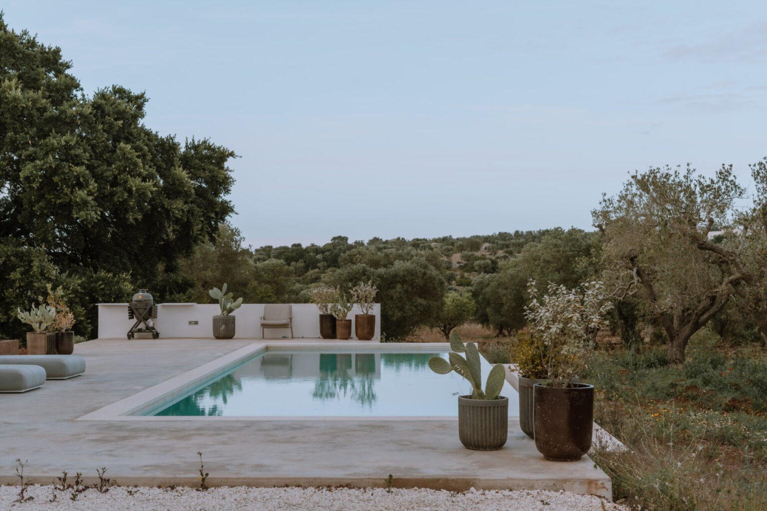 Modern outdoor swimming pool surrounded by lush greenery and decorative potted plants, offering a serene landscape view. Ideal for relaxation and luxury living. | Only on SopranoVillas