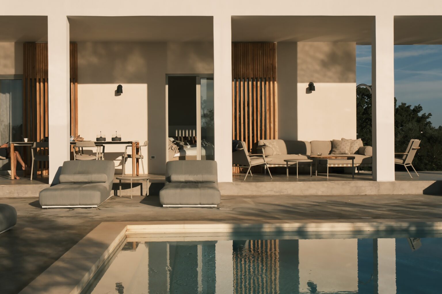 Modern villa with a private pool, featuring stylish outdoor lounge chairs and a dining area, surrounded by sleek architecture and natural light. Ideal for luxury vacations and relaxation. | Only on SopranoVillas