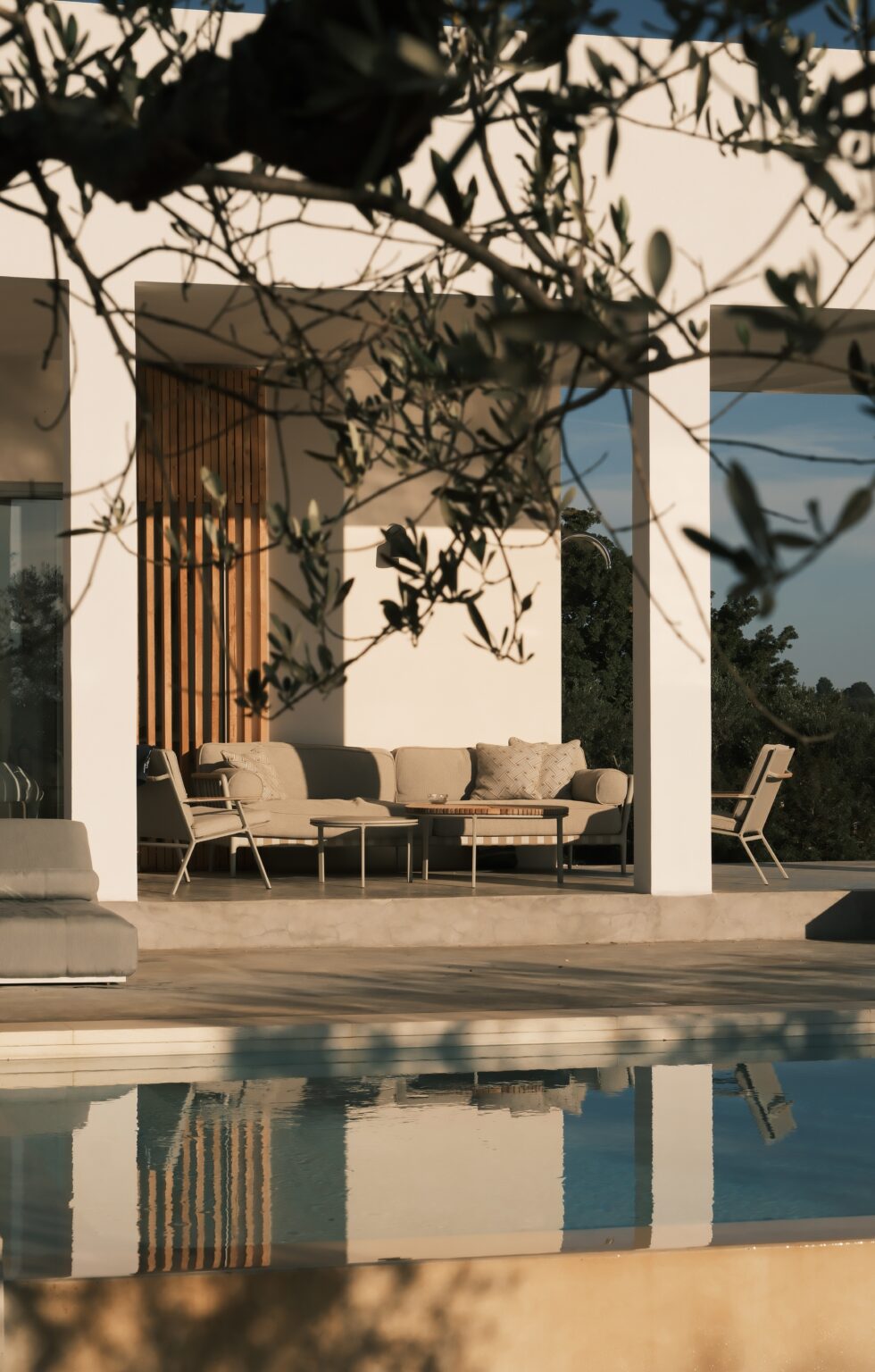 Modern outdoor living space featuring stylish beige furniture and wooden accents, framed by olive branches and a serene landscape in the background. | Only on SopranoVillas