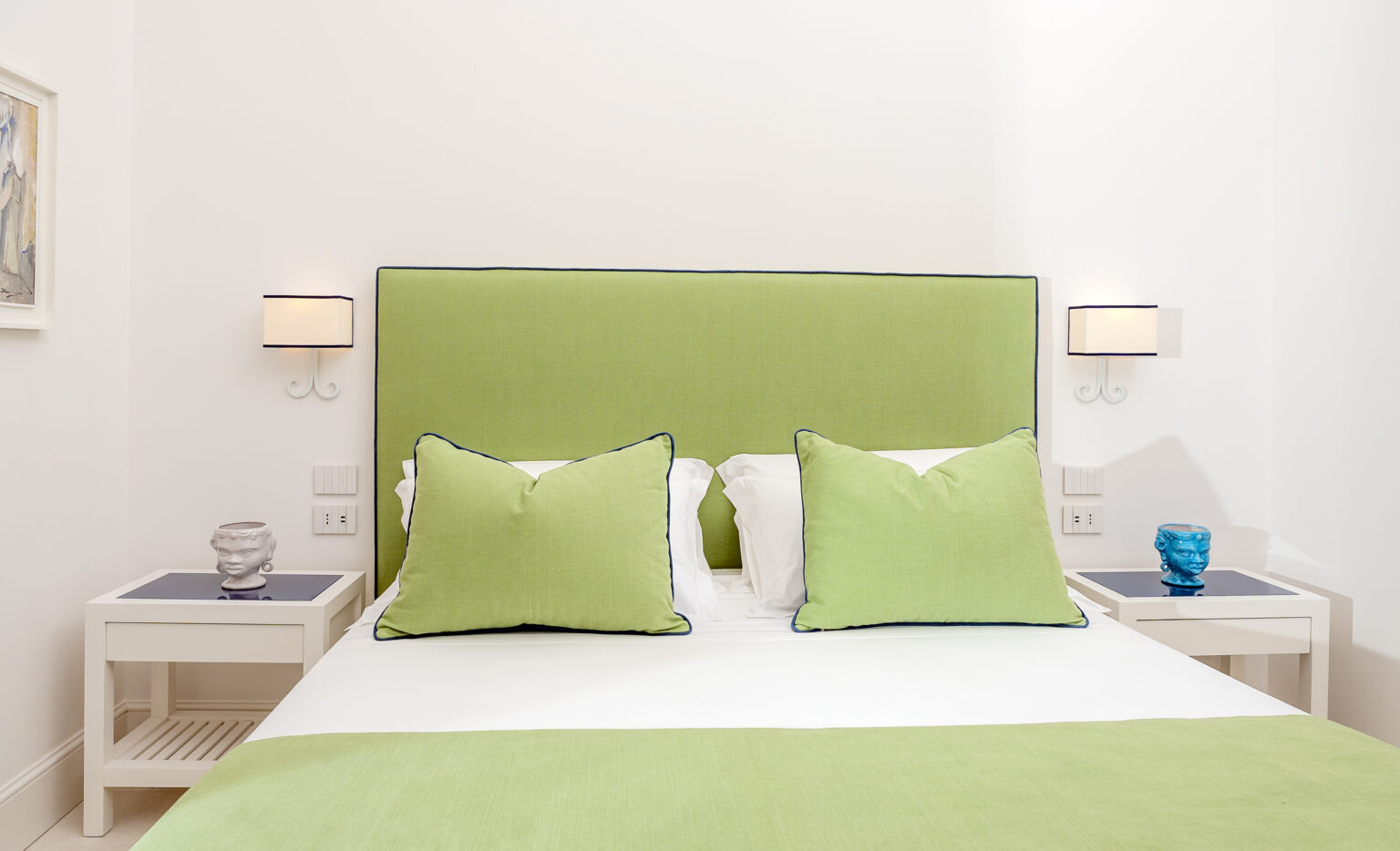 Cozy bedroom featuring a green upholstered headboard, white bedding, and decorative pillows, complemented by stylish bedside lamps and modern decor. Ideal for a relaxing atmosphere. | Only on SopranoVillas