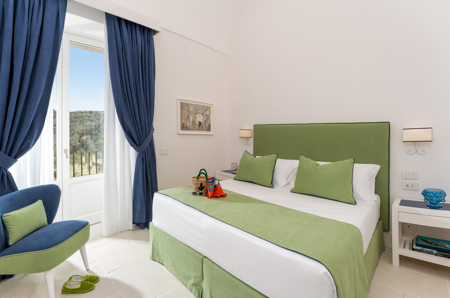 Bright and modern hotel bedroom featuring a green bedspread, blue curtains, and stylish decor, with a view of nature through the window. Ideal for a relaxing getaway. | Only on SopranoVillas