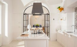 Modern kitchen featuring a spacious island, sleek white cabinetry, and a stylish black hood. The open layout includes decorative elements like fresh flowers and vibrant accents, creating a bright and inviting atmosphere.