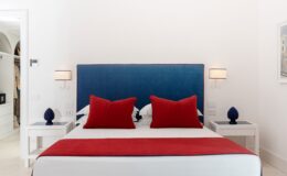 Modern bedroom featuring a blue upholstered headboard, red decorative pillows, and white nightstands with blue lamps, creating a stylish and inviting atmosphere.