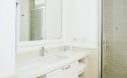Modern bathroom interior featuring a sleek white sink, vanity with storage, and a glass shower enclosure. Natural light enhances the clean design, complemented by neutral tile and soft towels. Ideal for a relaxing and stylish space.