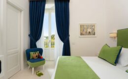 Modern bedroom interior featuring green accents, blue curtains, and a cozy chair, with natural light streaming through a large window. Ideal for showcasing stylish home decor and comfortable living spaces.