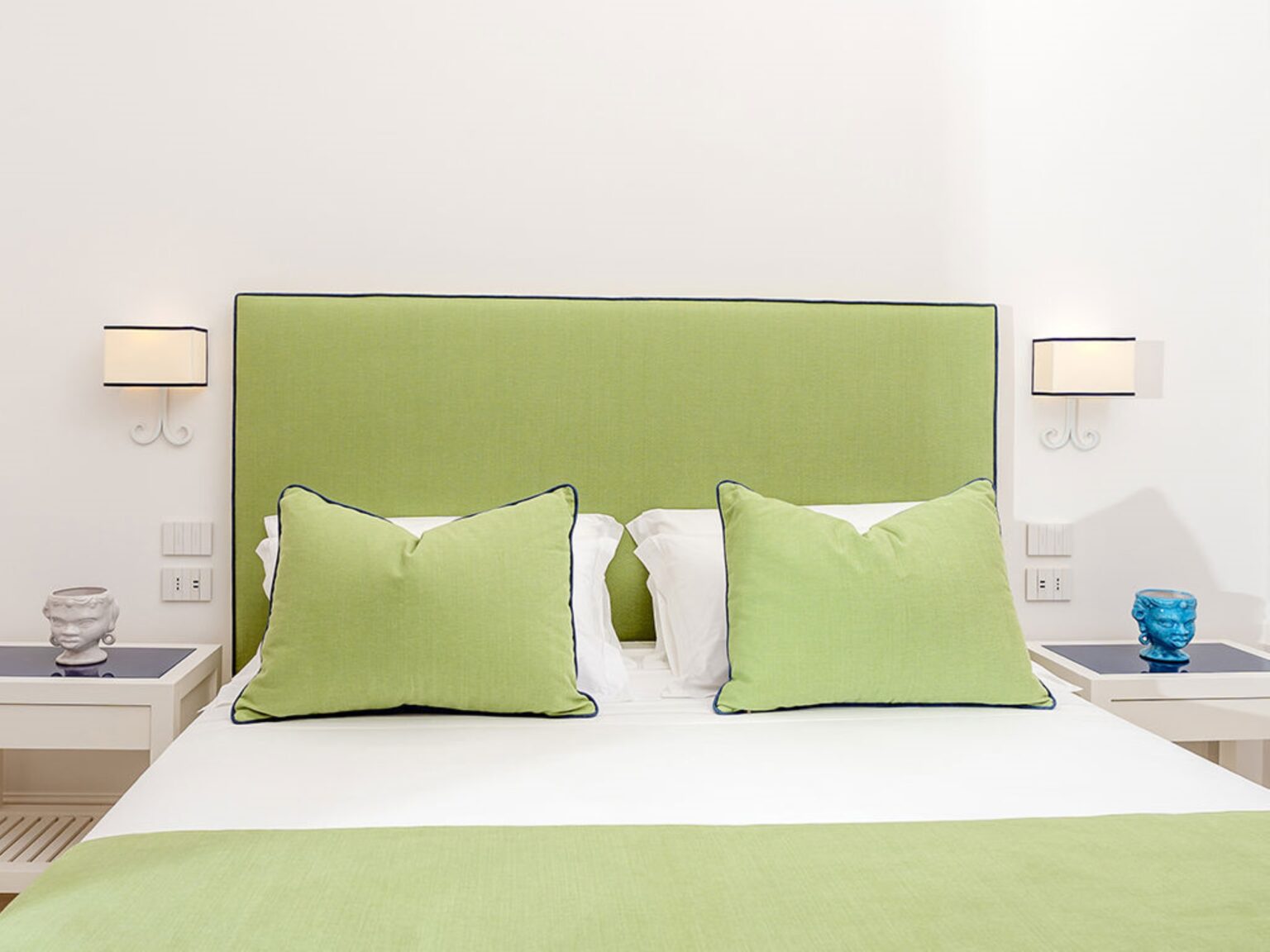 Modern bedroom featuring a green upholstered headboard with large matching pillows, white bedding, and stylish bedside lamps. Decorative blue and white accents enhance the contemporary decor. Ideal for a relaxing retreat. | Only on SopranoVillas