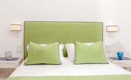 Modern bedroom featuring a green upholstered headboard with large matching pillows, white bedding, and stylish bedside lamps. Decorative blue and white accents enhance the contemporary decor. Ideal for a relaxing retreat.