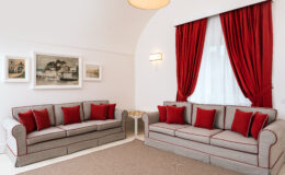 Modern living room featuring two gray sofas with red accent pillows, elegant red curtains, and framed artwork on the wall, creating a stylish and inviting atmosphere.