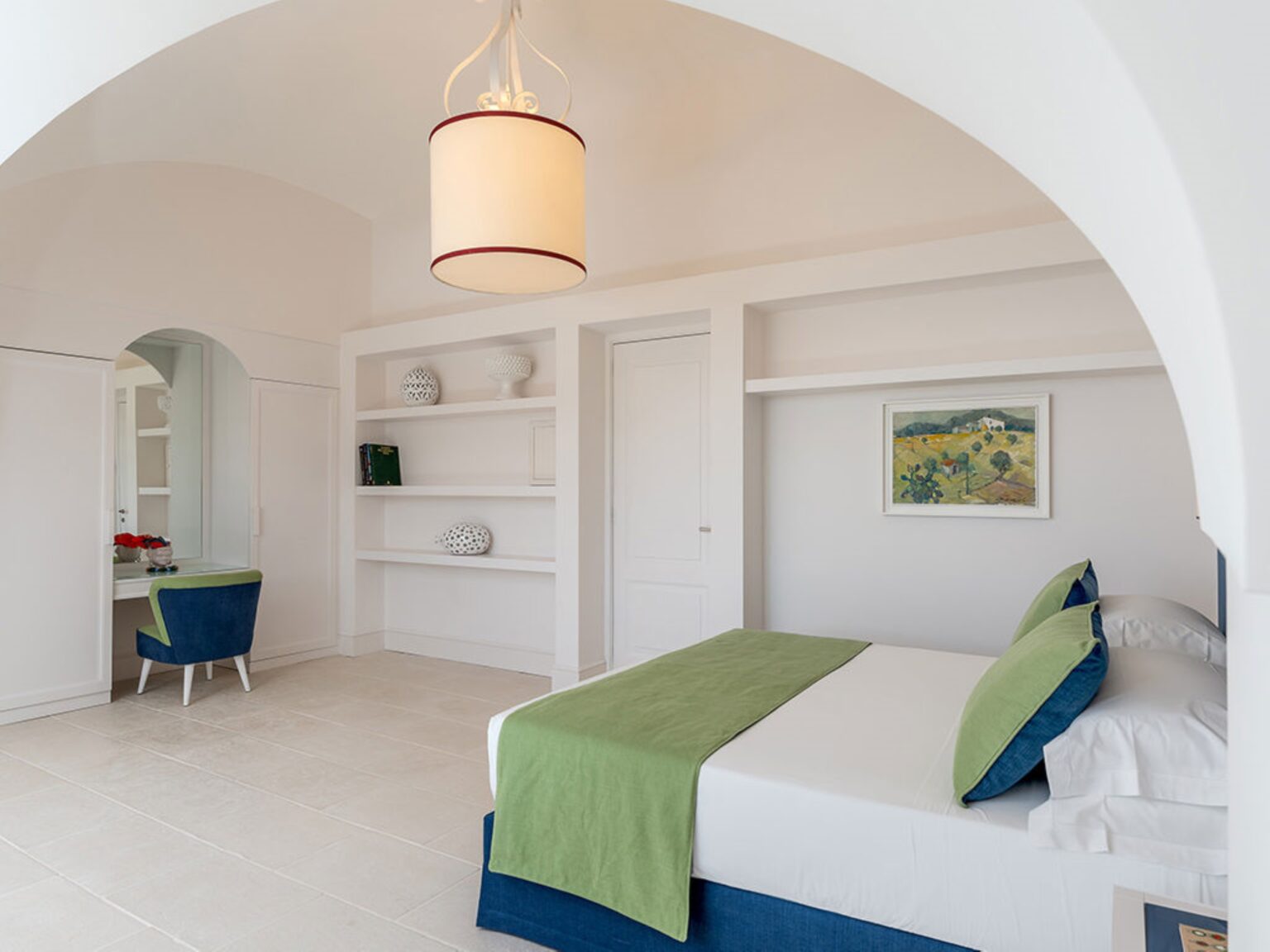 Modern bedroom interior featuring a white color scheme, a green-accented bed, a stylish pendant light, and a cozy workspace with a blue chair. The room includes built-in shelves and a door leading to another area, creating a spacious and inviting atmosphere. Ideal for relaxation and productivity. | Only on SopranoVillas