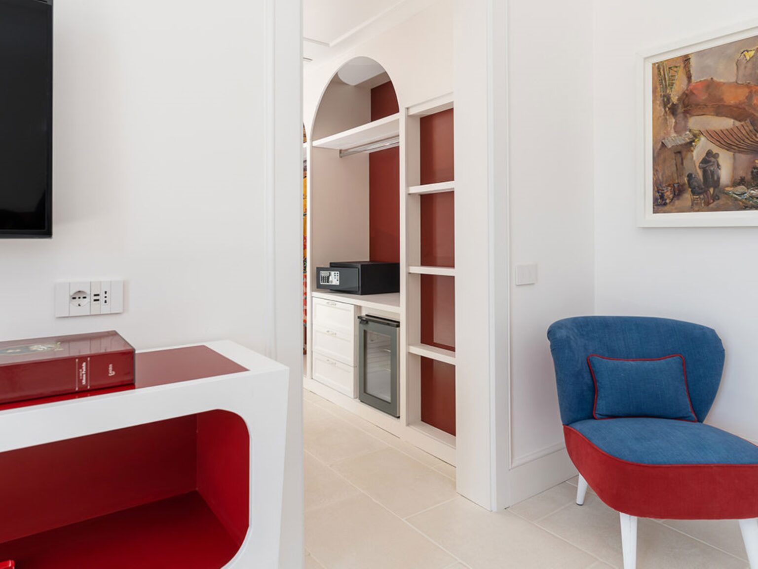 Interior view of a modern living space featuring an archway leading to a kitchenette with a microwave and shelves, complemented by a stylish blue chair and red accents. Ideal for showcasing contemporary home design and functionality. | Only on SopranoVillas