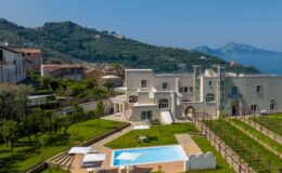 Luxury villa with a swimming pool, surrounded by lush greenery and mountains, overlooking the sea. Ideal for relaxation and scenic views in a Mediterranean setting.