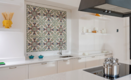 Modern kitchen interior featuring a stylish backsplash with floral pattern, stainless steel pots on a sleek countertop, and minimalist white cabinetry. Decorative items include a yellow vase with pasta and turquoise cookware, creating a vibrant and inviting atmosphere.