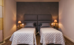 Modern hotel room featuring two single beds with gray upholstered headboards, soft lighting from bedside lamps, and a minimalist design. Ideal for travelers seeking comfort and style.