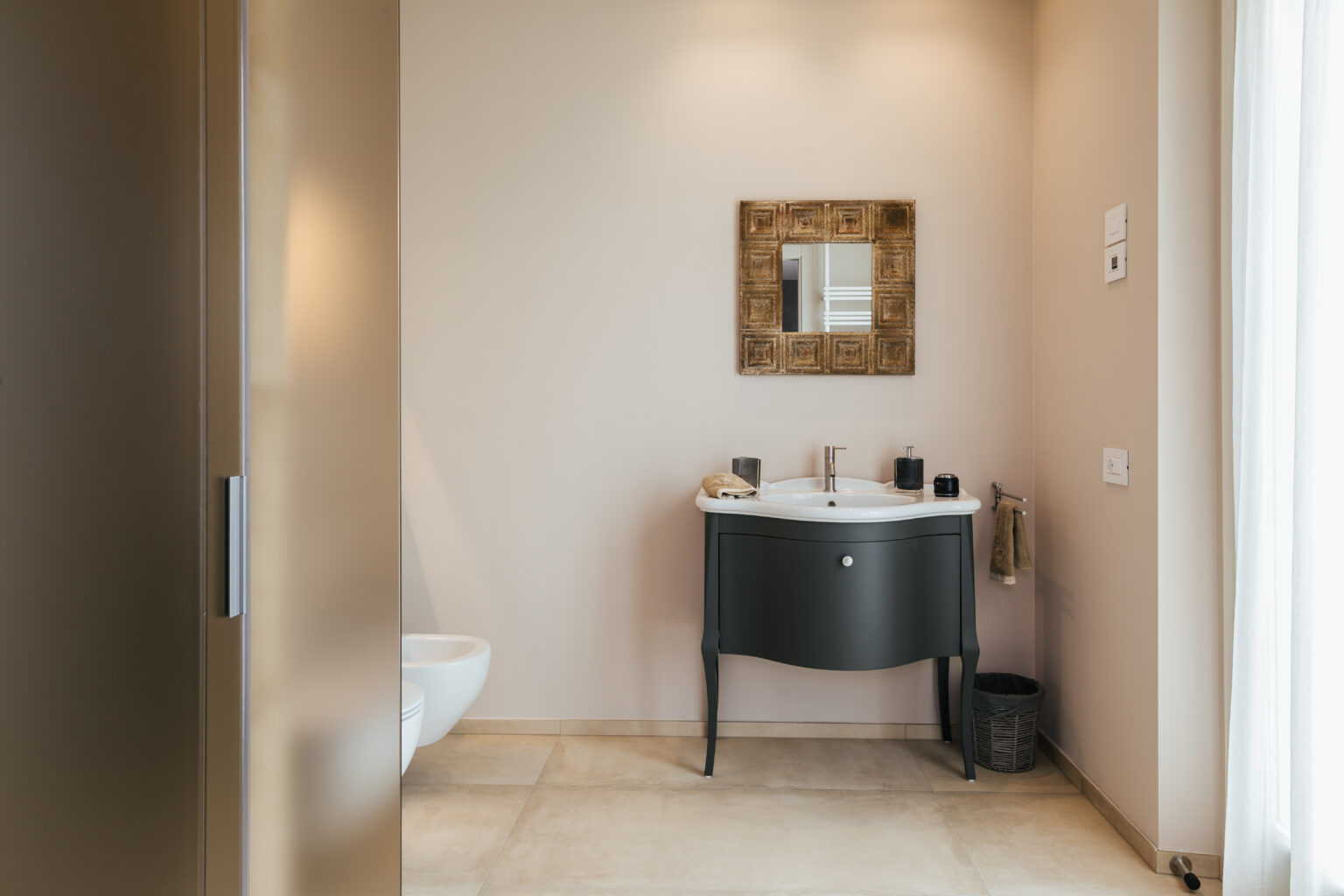 Modern bathroom interior featuring a sleek black vanity, a stylish mirror, and neutral wall colors. The space is well-lit with natural light, showcasing elegant tile flooring and minimalistic decor. | Only on SopranoVillas