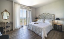Cozy and elegant bedroom featuring a plush white bed with decorative headboard, large windows with scenic views, and stylish furnishings including a mirror and side tables, perfect for a relaxing getaway.
