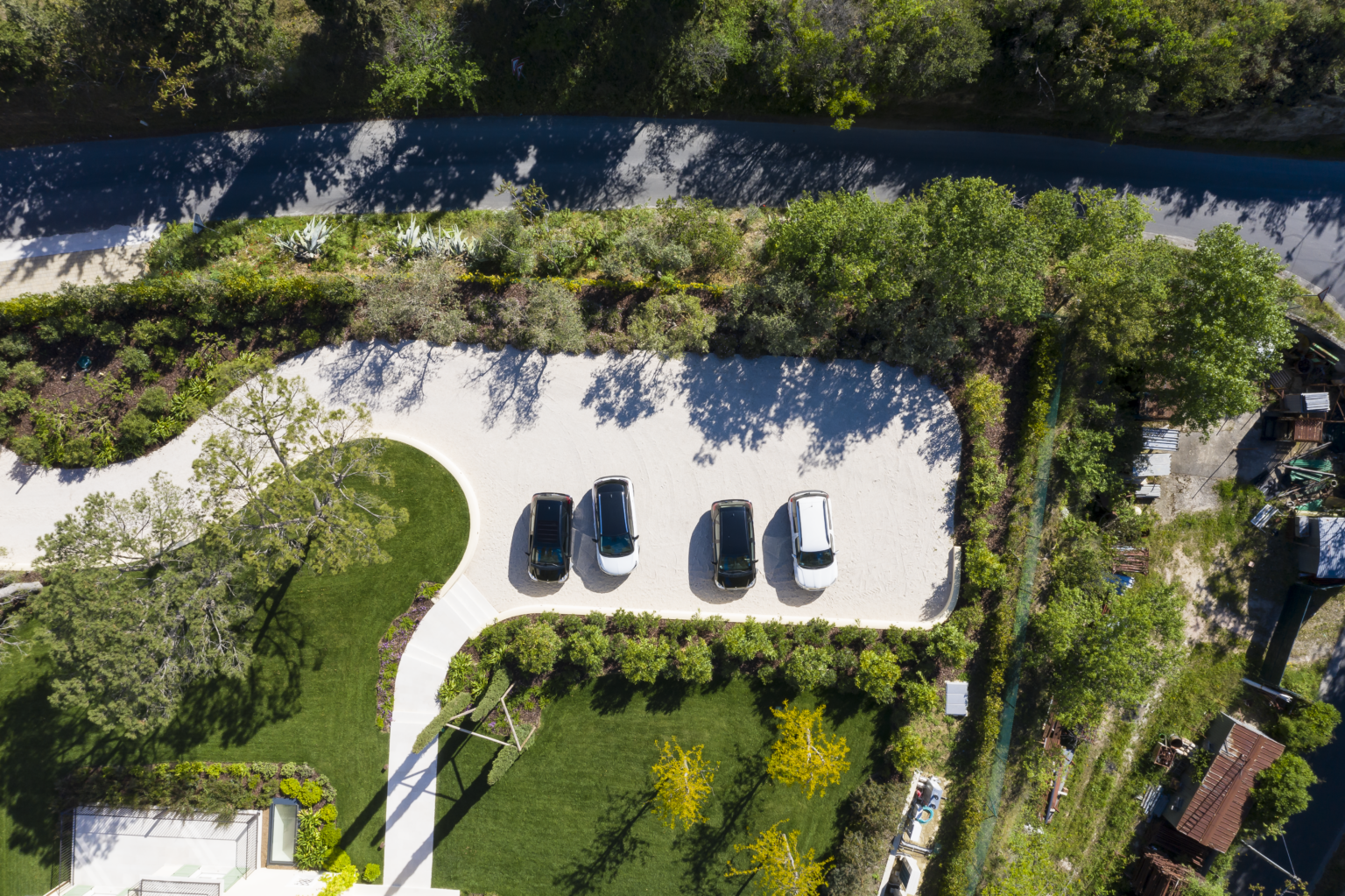 Aerial view of a landscaped parking area featuring four parked vehicles surrounded by greenery and trees, with a winding road in the background. | Only on SopranoVillas