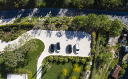 Aerial view of a landscaped parking area featuring four parked vehicles surrounded by greenery and trees, with a winding road in the background.
