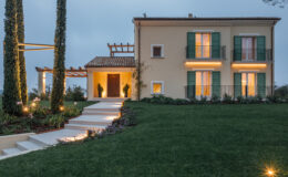 Elegant two-story house with green shutters, surrounded by landscaped gardens and illuminated pathways, showcasing modern architecture against a twilight sky.