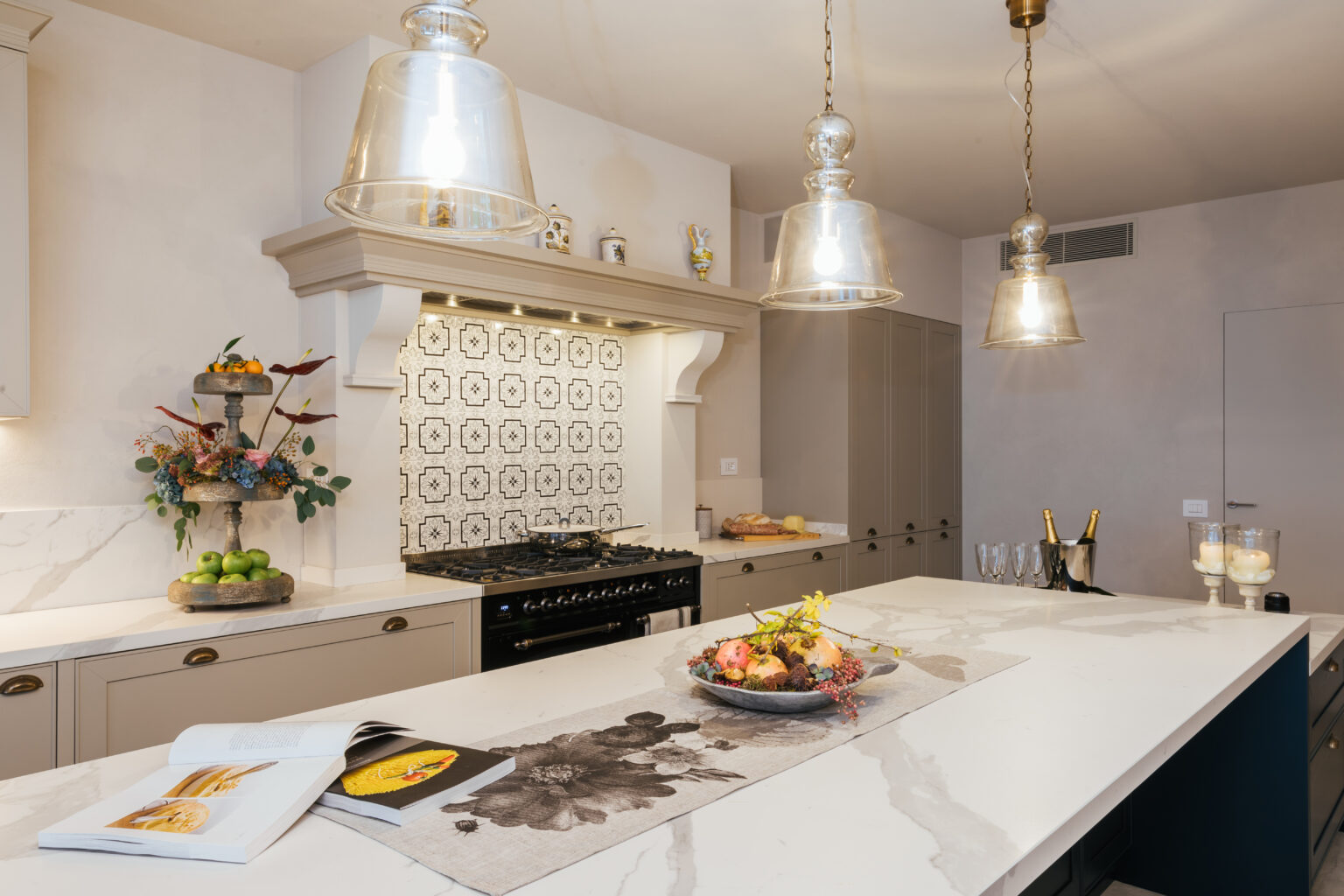 Modern kitchen featuring a large marble island, stylish pendant lighting, and a decorative backsplash. The space is complemented by a gas range, elegant cabinetry, and a fresh fruit display, creating a functional and inviting atmosphere. | Only on SopranoVillas