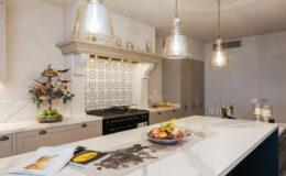 Modern kitchen featuring a large marble island, stylish pendant lighting, and a decorative backsplash. The space is complemented by a gas range, elegant cabinetry, and a fresh fruit display, creating a functional and inviting atmosphere.