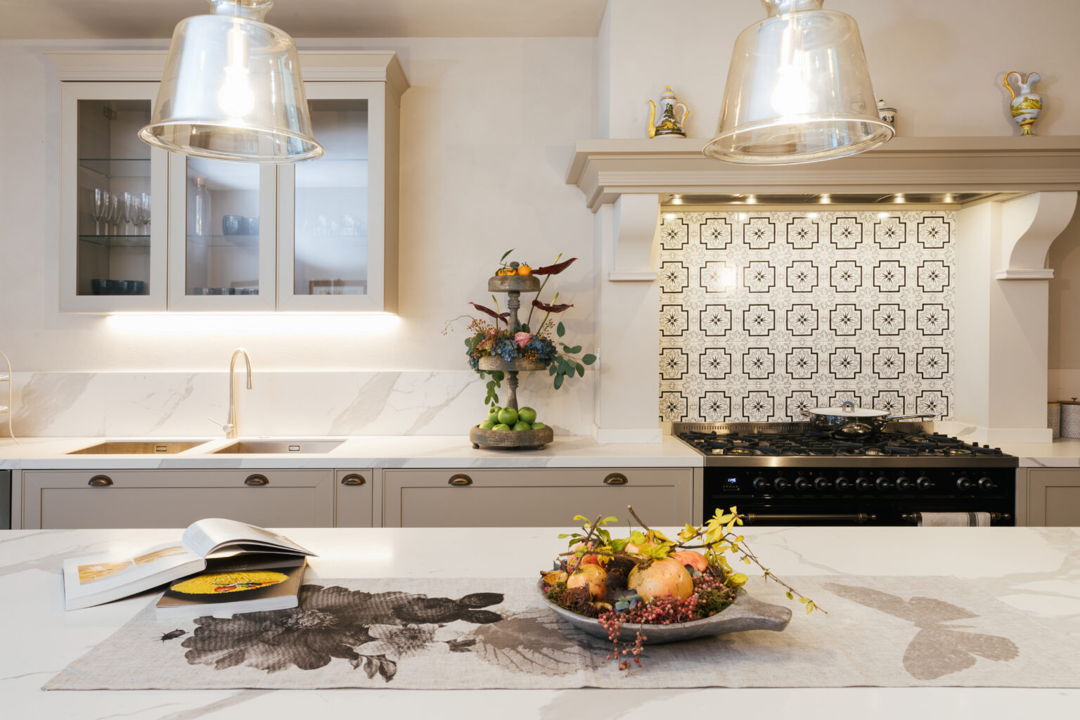 Modern kitchen interior featuring a large island with a decorative fruit bowl, elegant pendant lighting, and stylish patterned backsplash. The design showcases a blend of contemporary and classic elements, with a focus on functionality and aesthetics. | Only on SopranoVillas