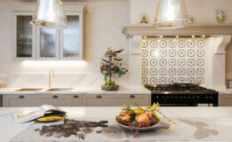 Modern kitchen interior featuring a large island with a decorative fruit bowl, elegant pendant lighting, and stylish patterned backsplash. The design showcases a blend of contemporary and classic elements, with a focus on functionality and aesthetics.