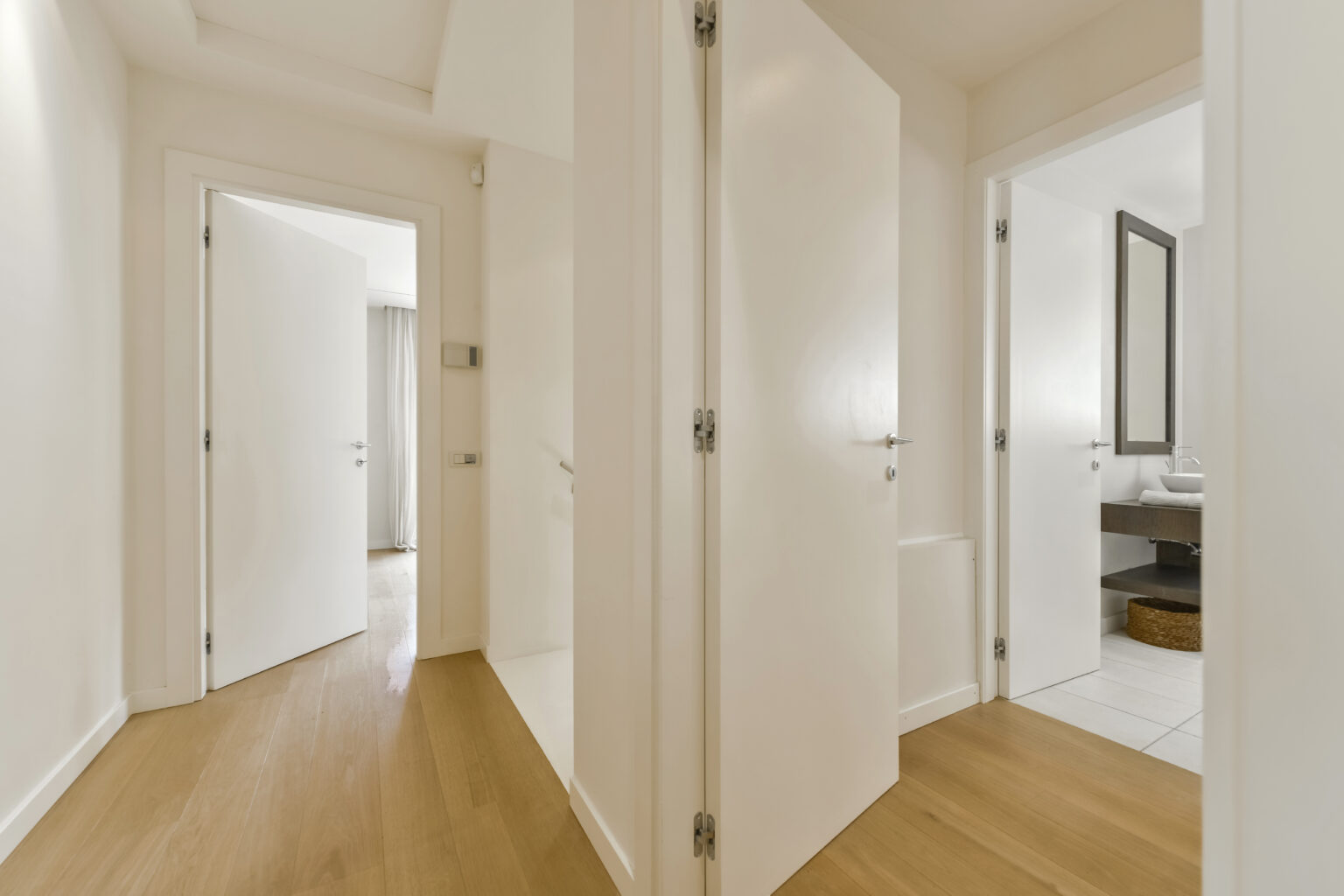 Modern interior hallway featuring two open doors leading to adjacent rooms, with light-colored walls and wooden flooring, creating a spacious and inviting atmosphere. | Only on SopranoVillas