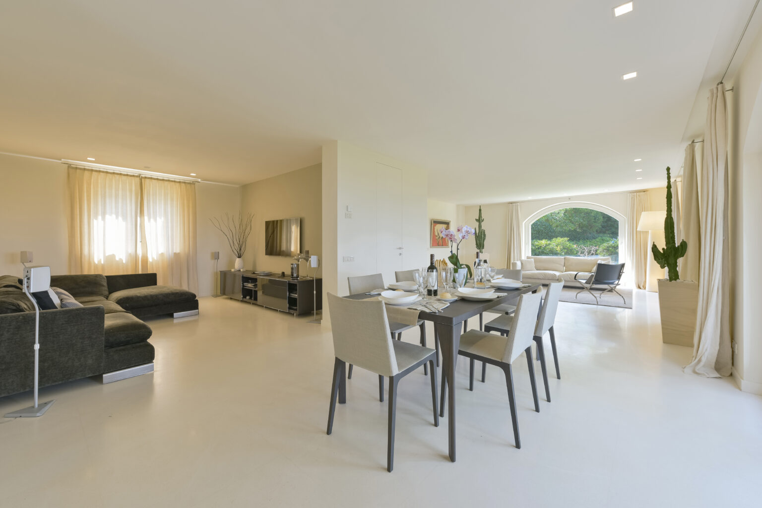 Modern open-plan living and dining area featuring a sleek dining table with chairs, a comfortable sofa, and large windows that provide natural light and views of the outdoors. | Only on SopranoVillas