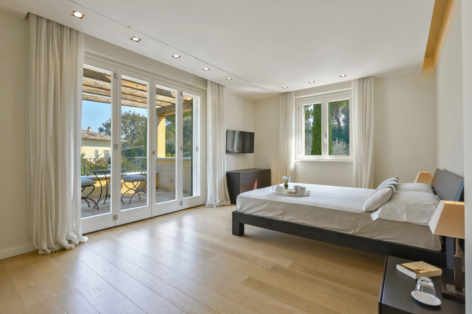 Bright and airy bedroom featuring large windows with a view of the outdoors, modern furnishings, a comfortable bed, and wooden flooring, ideal for relaxation and comfort. | Only on SopranoVillas