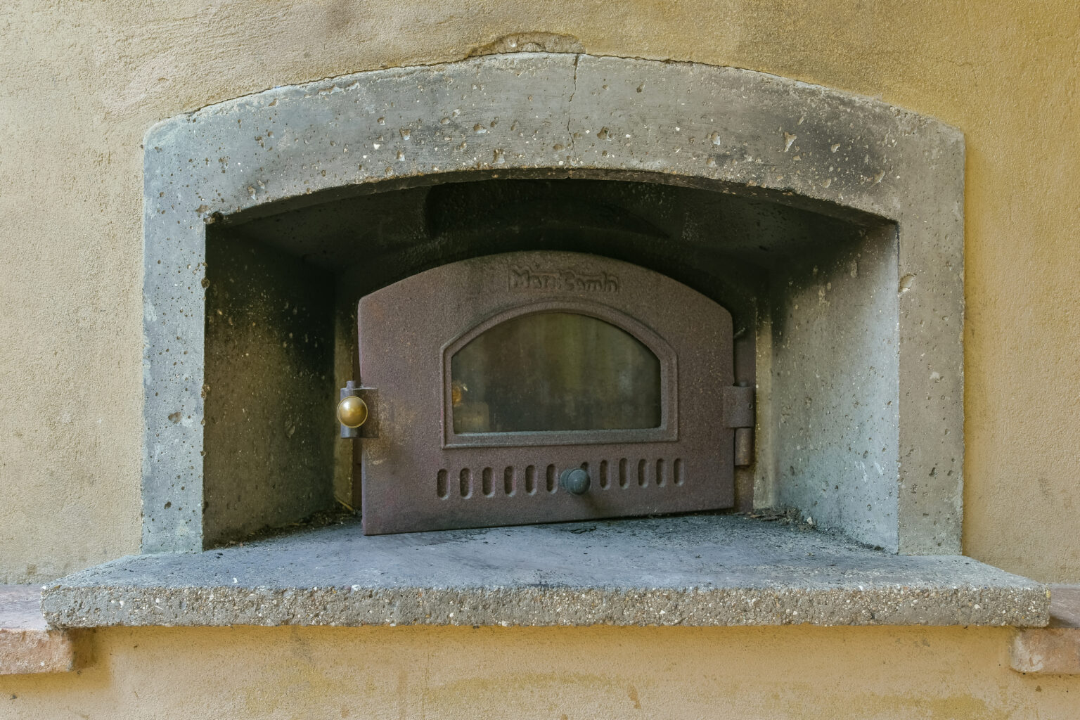 Rustic stone oven with a metal door, set into a textured wall, ideal for traditional baking and cooking. | Only on SopranoVillas
