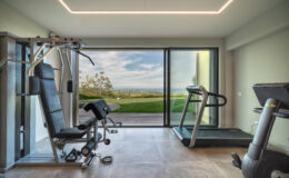Modern home gym featuring a treadmill and multi-gym equipment, with large windows offering a scenic view of greenery and a bright, airy atmosphere. Ideal for fitness enthusiasts looking to exercise in a stylish environment.
