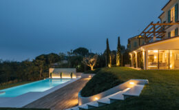 Modern villa exterior at dusk featuring a beautifully lit swimming pool, landscaped garden, and elegant architectural design, surrounded by lush greenery.