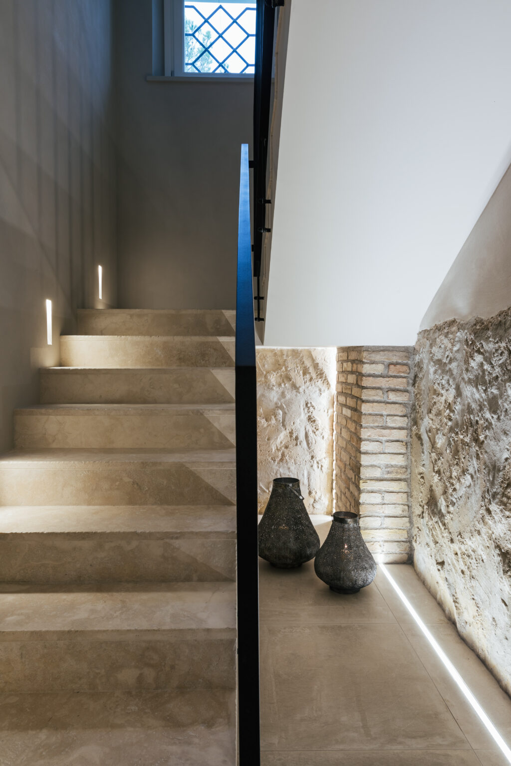 Modern staircase with soft lighting and textured stone walls, showcasing a blend of contemporary design and natural materials. The image features illuminated steps leading to a minimalist space, emphasizing the aesthetic appeal of the architectural elements. | Only on SopranoVillas