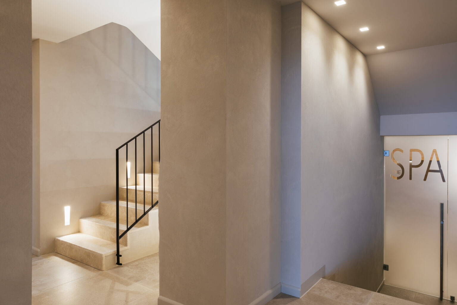 Modern spa entrance featuring minimalistic design with a staircase leading to upper levels, soft lighting, and a clear "SPA" sign on the wall. | Only on SopranoVillas