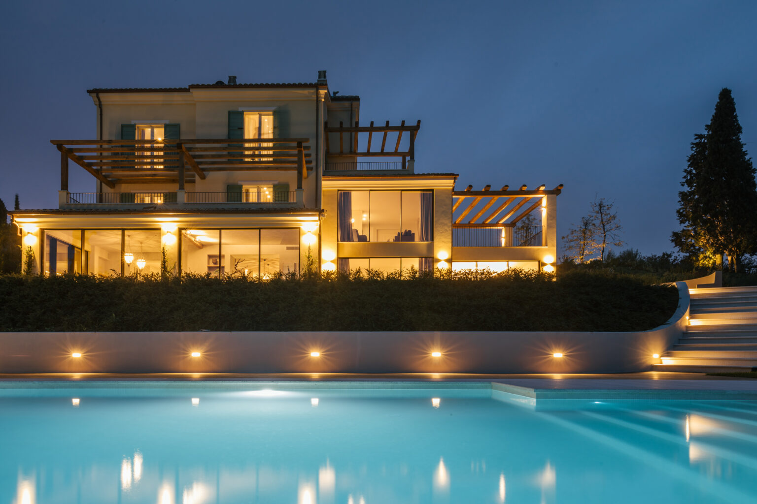 Luxurious modern villa at night with illuminated pool, featuring a spacious terrace and landscaped garden. | Only on SopranoVillas