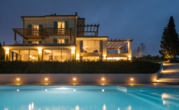 Luxurious modern villa at night with illuminated pool, featuring a spacious terrace and landscaped garden.