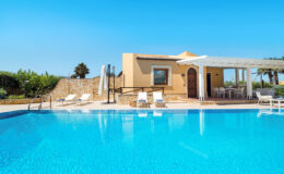 Modern villa with private swimming pool, surrounded by lush greenery and sun loungers, perfect for a relaxing getaway.