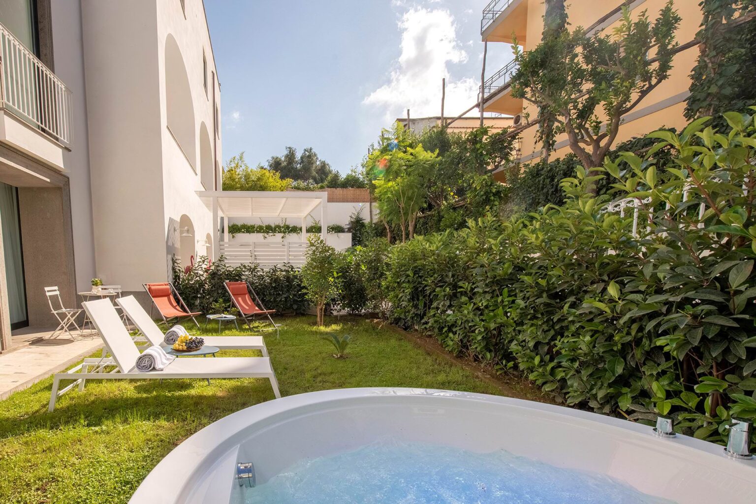 Relaxing outdoor space featuring a hot tub, sun loungers, and lush greenery in a serene garden setting, ideal for leisure and relaxation. | Only on SopranoVillas